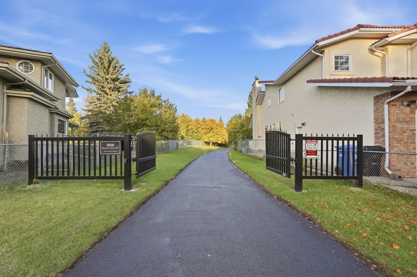 Private gated entrance and tree-lined driveway leading to 1008 Shawnee Drive SW, Calgary